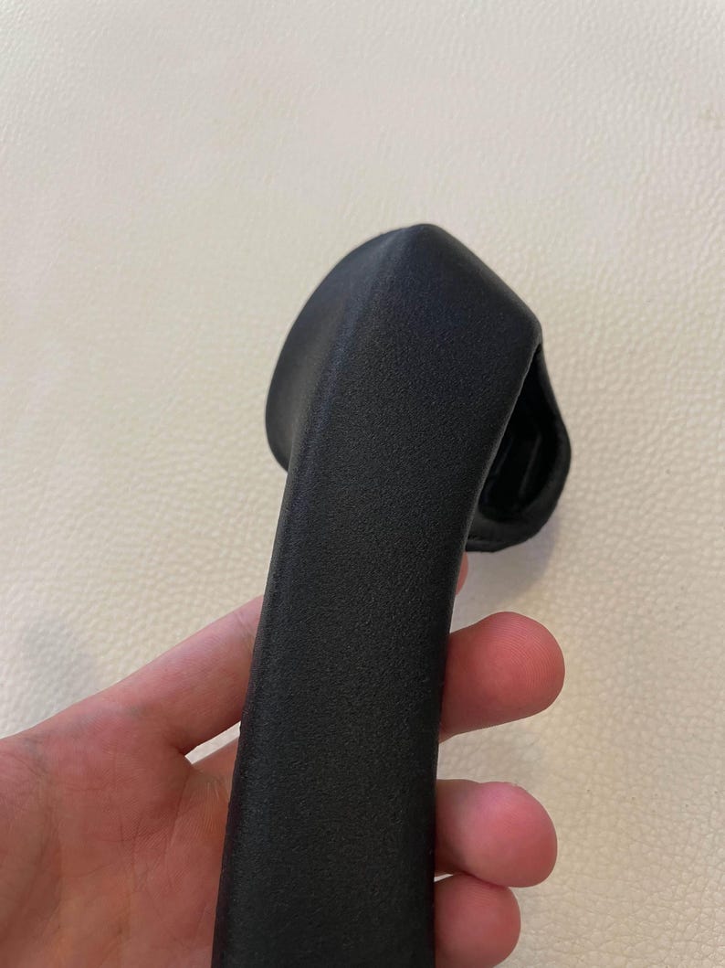 May include: A black, textured, curved handle with a matte finish. The object features a solid, elongated grip section that tapers slightly toward the top, with a wider, rounded base component visible at the upper end of the structure.