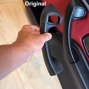 May include: A comparison of two black car door handles. One handle is labeled Original and shows significant damage with a broken section. The other handle is labeled Reinforced and appears intact and fully functional, mounted on a red and black door panel.