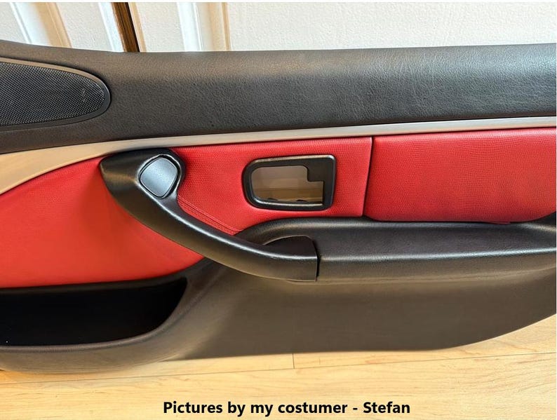 May include: A car door panel featuring a black upper and lower section with a central red leather insert. The panel includes a black door handle, a black interior door release lever, and a speaker grille. Text at the bottom reads: Pictures by my costumer - Stefan