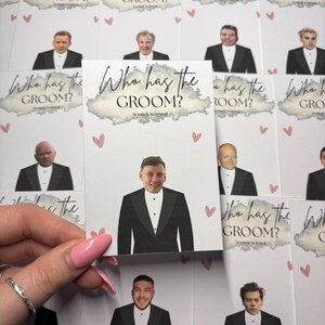 May include: A collection of rectangular game cards titled Who has the GROOM? with the instruction Scratch to reveal. Each white card features a printed illustration of a person in a black tuxedo and small pink hearts scattered across the surface.