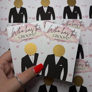 May include: A collection of rectangular game cards featuring the text Who has the GROOM? Scratch to reveal. Each card displays a black tuxedo illustration with a circular gold scratch-off sticker where the head would be, accented by pink hearts.