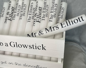 May include: A white wooden crate containing multiple white foam glow sticks. Each glow stick is printed with the text 'Mr & Mrs Elliott' and '04.10.25'. The front of the crate features the text 'Grab a Glowstick' and 'get on the dancefloor'.