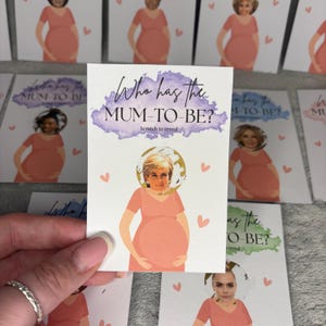 May include: A rectangular game card featuring the text Who has the MUM-TO-BE? Scratch to reveal. The card displays a graphic of a person in a peach-coloured dress with a round scratch-off area over the head, revealing a portrait of a person.