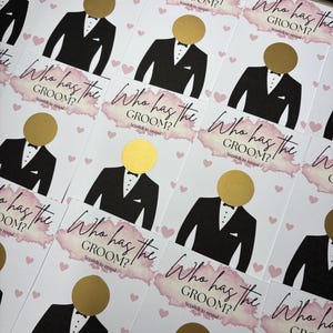 May include: A collection of rectangular game cards featuring the text Who has the GROOM? Scratch to reveal. Each card displays a black tuxedo illustration with a circular gold scratch-off sticker for the head, accented by pink watercolour and hearts.