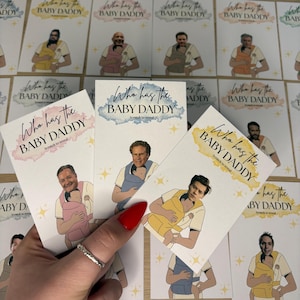May include: Cards with the text "Who has the BABY DADDY" and "Scratch to reveal". The cards feature illustrations of men holding babies in carriers. The cards have a watercolor effect in pink, blue, and yellow.
