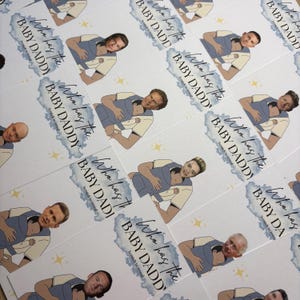 May include: Cards with illustrations of men holding babies in carriers. The cards have the text "Who has the BABY DADDY? Scratch to reveal" in a blue watercolor design. The cards are white with yellow star accents.