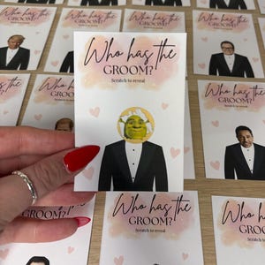 May include: A rectangular game card featuring the text Who has the GROOM? Scratch to reveal in black script and sans-serif font. The card displays a graphic of a tuxedo-clad figure with a circular scratch-off area revealing Shrek's face.