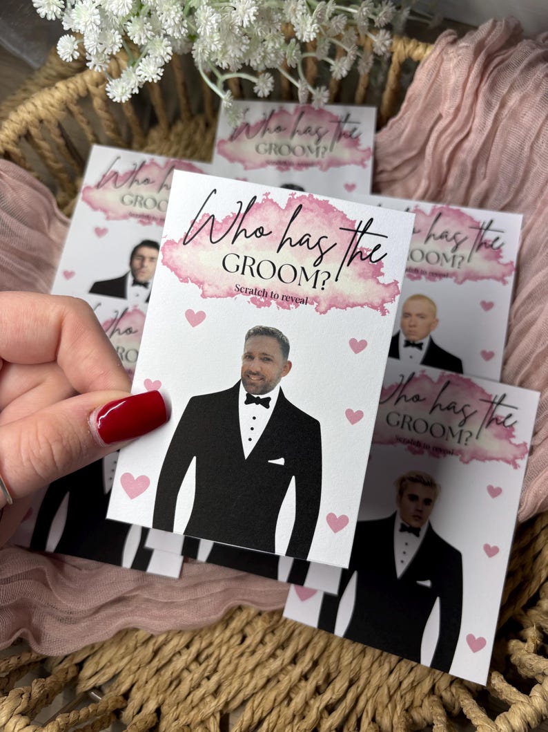 May include: A rectangular game card featuring the text Who has the GROOM? Scratch to reveal in pink watercolour script and black font. The card displays a graphic of a man in a black tuxedo with a bow tie, surrounded by small pink hearts.