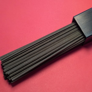 May include: A close-up of a bundle of black spaghetti noodles in a black box on a red background.