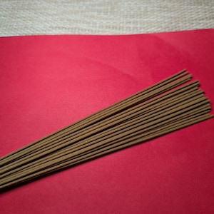 May include: A bundle of brown incense sticks on a red surface.