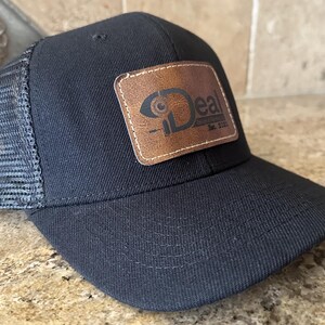 May include: Black trucker hat with a brown leather patch that says "Deal" in a stylized font. The patch has a small circle with a line through it.