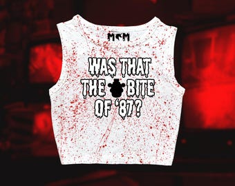 May include: White crop top with a red splatter design. The text "WAS THAT THE BITE OF '87?" is printed in black, with a black bear graphic. The top has a scoop neck and is sleeveless.