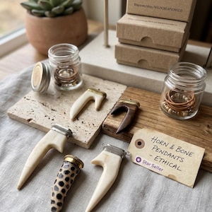 May include: A collection of five horn and bone pendants with metal caps, arranged alongside two small glass jars containing small beads and a tag labeled Horn & Bone Pendants - ETHICAL Star Seller. The pendants feature various shapes, including smooth cream-colored, dark brown, and a spotted pattern.