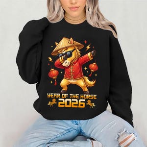 Può includere: Felpa nera con una grafica colorata di un cavallo che fa dab, con occhiali da sole e un cappello conico. Il cavallo indossa una giacca rossa. Il testo "YEAR OF THE HORSE 2026" è sotto.