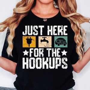 May include: Black t-shirt with white text that reads "Just Here For The Hookups" with a graphic of an electrical outlet, a faucet, and a camper van.