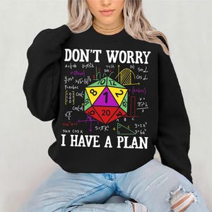 Könnte beinhalten: Schwarzes Sweatshirt mit dem Text "DON'T WORRY I HAVE A PLAN" und mathematischen Formeln. Ein farbenfroher 20-seitiger Würfel befindet sich in der Mitte. Ein lässiges, bequemes Kleidungsstück.