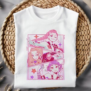 May include: White t-shirt featuring a colorful anime-style graphic. The graphic depicts three female characters in a comic book panel design, with names "Miha", "Rumi", and "Zoey". The artwork uses pink, purple, and red hues.