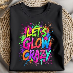 May include: Black crew neck t-shirt with the phrase "LET'S GLOW CRAZY" in a vibrant, multicolored, graffiti-style design. The text is surrounded by colorful paint splatters in shades of green, pink, blue, orange, and purple.