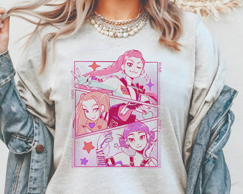 May include: A light gray t-shirt featuring a manga-style graphic with three female characters in a comic strip layout. The characters have pink, light brown, and purple hair. The names "MIRA", "RUMI", and "ZOEY" are printed on the side.