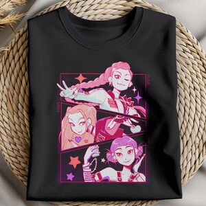 May include: Black t-shirt featuring a colorful anime-style illustration of three girls. The artwork includes pink, purple, and white accents, with the names "Mira" and "Humi" visible. The design is set against a background of stars.