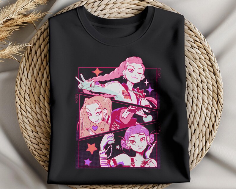May include: Black t-shirt featuring a colorful anime-style illustration of three girls. The artwork includes pink, purple, and white accents, with the names "Mira" and "Humi" visible. The design is set against a background of stars.