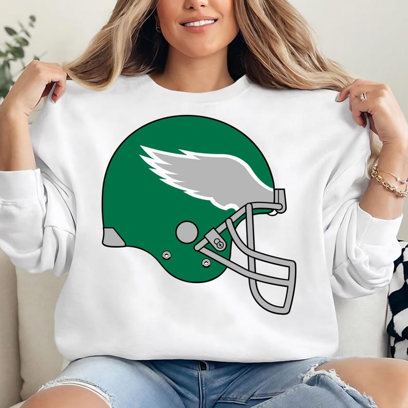 May include: White sweatshirt with a green and gray football helmet graphic. The helmet has a wing design on the side.