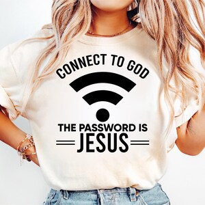 May include: Cream-colored t-shirt with the text "CONNECT TO GOD" above a black Wi-Fi symbol. Below the symbol, the text reads "THE PASSWORD IS JESUS" in a bold, black font. The shirt is a casual, everyday wear item.