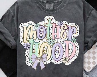 May include: Dark gray sweatshirt with the word "MOTHERHOOD" in a colorful, retro font. The design includes pastel flowers, hearts, and a bow, all set against a white cloud-shaped background with black speckles. A casual, comfortable top.