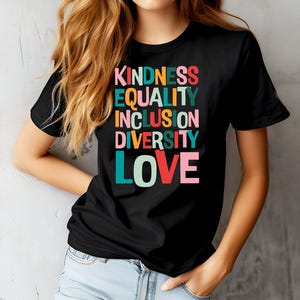 May include: Black t-shirt with the words "KINDNESS, EQUALITY, INCLUSION, DIVERSITY, LOVE" in a colorful, stacked design. The shirt is a crew neck style.