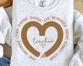 Può includere: Una felpa grigia con un design a forma di cuore di matita marrone. Il cuore contiene la parola "teacher". Le parole "Lead, Encourage, Listen, Teacher, Inspire, Love, Motivation, Dream, Connect, Future" sono scritte in un cerchio attorno al cuore.