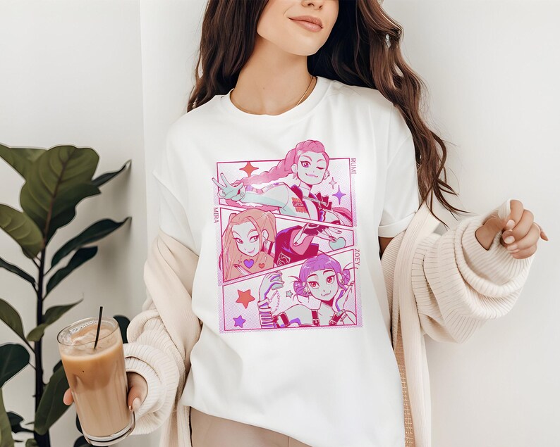 May include: White t-shirt featuring a manga-style graphic in pink and purple. The design is divided into three panels, each showcasing a different character with text labels. The shirt is a casual, everyday wear item.