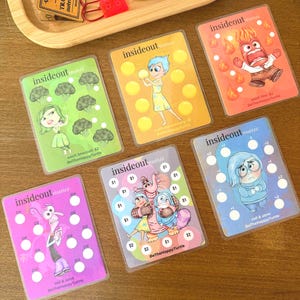 May include: A collection of six Inside Out Mini cards featuring characters like Joy, Sadness, and Anger. Each card has a unique design with character illustrations, circles, and text. The cards are in clear plastic sleeves.