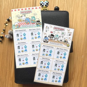 May include: Two colorful stickers featuring cartoon characters from the "HAPIDANBUI Cooking Challenge" series. The stickers have text and illustrations, with categories like "Best Overall Dish" and "Best Taste/Flavor". The stickers are on a black wallet.