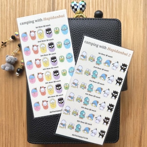 May include: Two sticker sheets with the text "camping with Hapidanbui" and "camping with Hapidanbui 2". The stickers feature colorful cartoon characters in various poses. The sheets are on a black leather wallet.