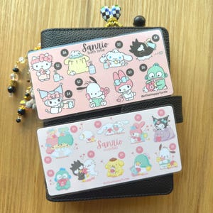May include: Two pink Sanrio character cards with the text "bath time" and "cuddles" are displayed on a black wallet. The cards feature various cartoon characters and price tags. A beaded charm is attached to the wallet.