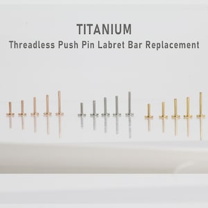 May include: An assortment of titanium threadless push pin labret bar replacements in various sizes. The image displays several rows of the labret bars in gold, silver, and rose gold colors. The text "TITANIUM" and "Threadless Push Pin Labret Bar Replacement" is displayed at the top.