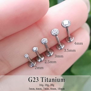 May include: Five silver-toned G23 titanium labret studs with clear round gemstones, arranged by size from 2mm to 4mm. The text G23 Titanium, 16g, 18g, 20g, and 5mm, 6mm, 7mm, 8mm, 10mm is printed below the jewelry, with individual labels for each stud.