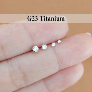 May include: Four G23 Titanium stud earrings with clear, round-cut stones arranged in a row by size from largest to smallest. Each stud features a prong setting that secures the sparkling white stone, creating a simple and clean aesthetic.