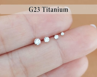 May include: Four G23 Titanium stud earrings with clear, round-cut stones arranged in a row by size from largest to smallest. Each stud features a prong setting that secures the sparkling white stone, creating a simple and clean aesthetic.