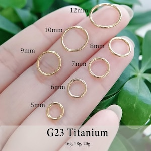 May include: A collection of seven gold-colored G23 titanium hoop rings in varying sizes labeled 5mm, 6mm, 7mm, 8mm, 9mm, 10mm, and 12mm. The text G23 Titanium and 16g, 18g, 20g is printed at the bottom of the image, indicating the gauge sizes.
