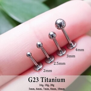 May include: Four silver-colored metal labret studs with spherical ends, arranged by size. The text G23 Titanium, 16g, 18g, 20g, and 5mm, 6mm, 7mm, 8mm, 10mm is visible. Individual ball sizes are labeled as 2mm, 2.5mm, 3mm, and 4mm.
