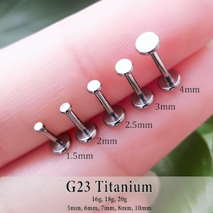 May include: Five silver-colored G23 titanium labret studs with flat circular tops, arranged by size from 1.5mm to 4mm. The text G23 Titanium, 16g, 18g, 20g, and 5mm, 6mm, 7mm, 8mm, 10mm is printed at the bottom of the image for reference.