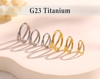 May include: A collection of six G23 Titanium hinged rings arranged in a row, featuring three silver-toned rings and three gold-toned rings of varying sizes. Each ring has a double-loop design with a smooth, polished finish and a secure hinge mechanism.