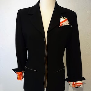 May include: A black blazer with a zip fastening and a patterned pocket square. The blazer has a long, fitted style and features a contrasting patterned lining on the cuffs.