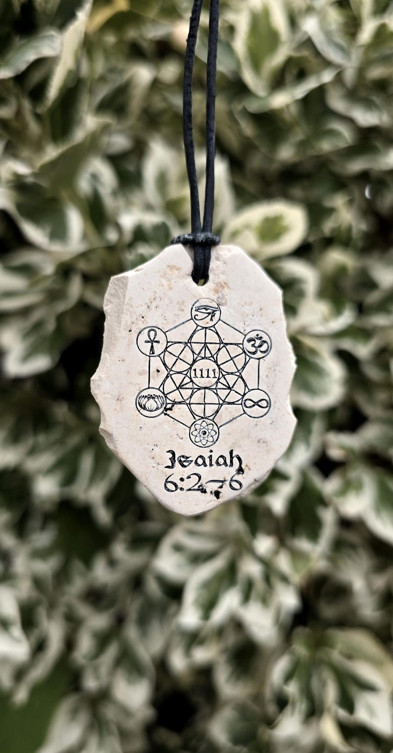 May include: A cream-colored, irregular stone pendant hanging from a black cord. The surface features a black ink print of a geometric Metatron's Cube design with various symbols, the number 1111, and the text Isaiah 6:2-6 printed at the bottom.