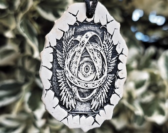 May include: A pendant featuring a central eye motif surrounded by intricate wings and circular patterns, rendered in black and white on a textured, off-white, irregularly shaped base, suspended from a simple black cord for wearing around the neck.
