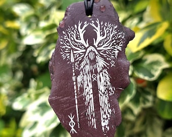 May include: A dark brown, irregularly shaped stone pendant hanging from a black cord. The stone features a white engraved illustration of a hooded figure with antlers, holding a long staff, surrounded by intricate tree-like branch patterns.