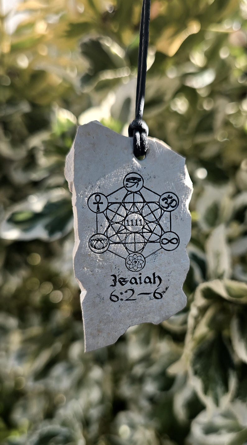 May include: A light gray, irregular stone pendant hanging from a black cord. The surface features a black printed design of a geometric Metatron's cube with various symbols, the number 1111, and the text Isaiah 6:2-6 printed in black ink.