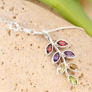 Könnte beinhalten: Eine silberne Halskette mit einem Anhänger in Form eines Zweigs mit Blättern. Die Blätter sind mit roten, violetten, gelben und grünen Edelsteinen besetzt.
