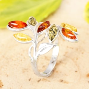May include: A silver ring with a leaf motif, set with amber-coloured stones. The ring's leaves display amber in shades of yellow, orange, and brown. The jewellery is set against a neutral backdrop, emphasising the ring's design and the amber's colours.